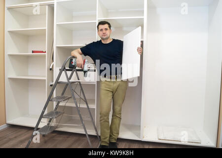Worker with a shelf near of big cabinet. Furniture installation. Stock Photo