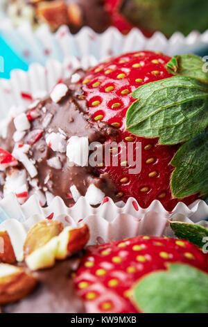 ripe strawberries dipped in  chocolate with nuts and caramel on blue background, close up Stock Photo