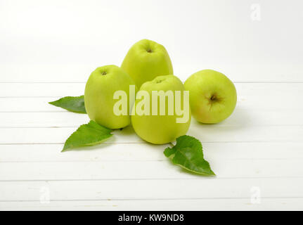 Four green apples with leaves on white wooden background Stock Photo