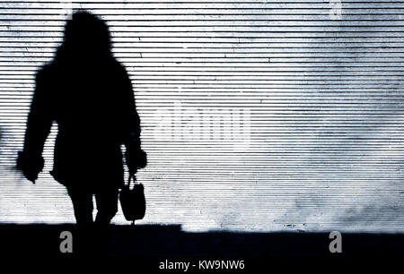 Blurry shadow silhouette of a woman walking the city street patterned sidewalk in the night in black and white Stock Photo