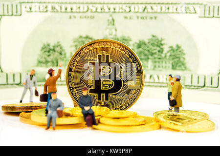 closeup of golden bitcoin coin on dollar banknote background with many golden coins at bottom and miniature figurines standing around Stock Photo