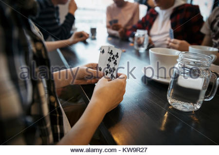 Close up tween boy playing cards with friends at cafe table