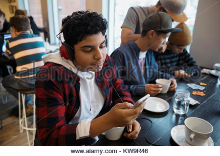 Middle Eastern tween boy with headphones listening to music with smart phone at cafe table