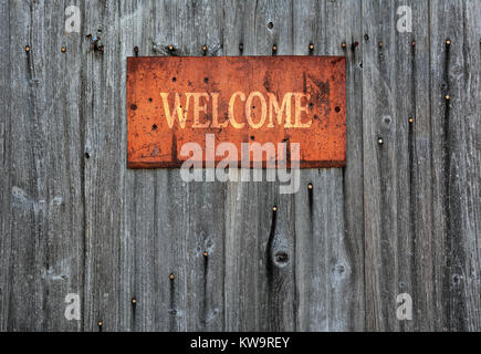 Rusty metal sign on wooden wall with the word Welcome. Stock Photo