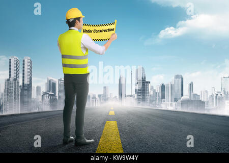 Back view of asian construction worker holding under construction signs in the road Stock Photo