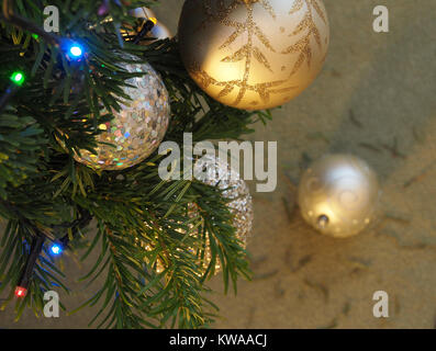Baubles and lights on a Christmas tree, with one bauble blurred on the floor with dropped pine needles. Stock Photo