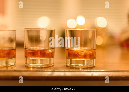 closeup of bourbon whiskey glasses with ice lined up on wood table with candles in background Stock Photo