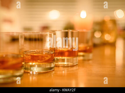 closeup of bourbon whiskey glasses on the rocks lined up on wood table with candles in background Stock Photo