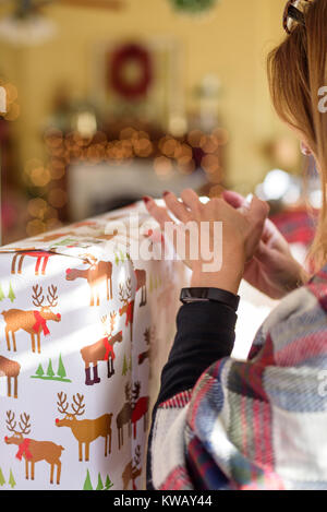 woman wrapping Christmas gift at home with bokeh lights in background Stock Photo