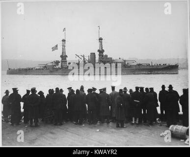 The US Naval leader Arizona cruises past the 96th Street Pier, where a group of men in hats and dark black coats stand facing it, New York, New York, 1918. Image courtesy National Archives. Stock Photo