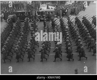 During a large parade honoring the return of the brave and heroic African American troops of the 369th Infantry, the old 15th of New York City, men march in tidy rows wearing uniform and holding rifles, with old cars and bystanders gathered on the side of Fifth Avenue, New York, New York, 1919. Image courtesy National Archives. Stock Photo