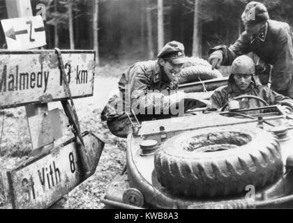 German SS troops with the 1st Panzer division check a highway sign at an Ardennes crossroad. One destination on the sign, Malmedy, would become the site of a Nazi massacre of 84 disarmed American POWs in the Battle of the Bulge. Still from a captured German film. Ca. Dec. 10-17, 1944. World War 2. (BSLOC 2014 10 91) Stock Photo