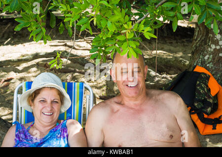 Old couple laughing on the beach, sitting, love. Stock Photo