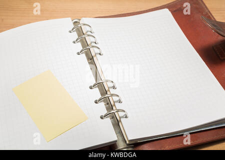 Binder of leather open on the table, with blank sheets for writting notes, and a post it on the other side. Stock Photo