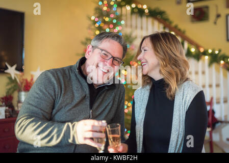 happy couple smiling and drinking champagne in front of Christmas tree at home Stock Photo