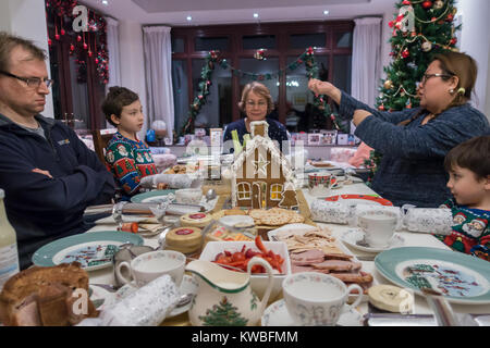 A mixed race family sit down at a dining table to enjoy a Christmas tea. Plates of cold meats, cheese and salad adorn the table. Stock Photo