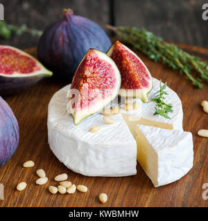 Camembert cheese with figs and pine nuts on wooden cutting board. Close up view, square composition Stock Photo
