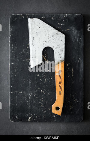 Old butcher axe or meat cleaver on black cutting board. Vertical, top view Stock Photo