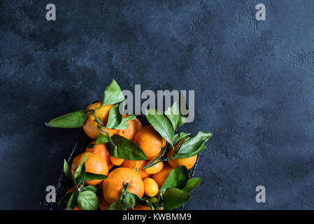 Fresh tangerines or clementines with green leaf in basket on dark stone background. Top view Stock Photo