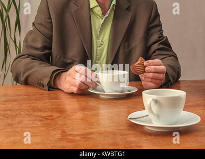 Business man talking shop and having coffee and cookie at desk with two cups Stock Photo