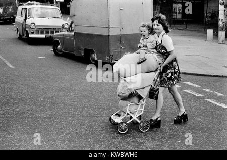 1970s poverty poor family London. Siblings teen girl pushing pram stacked with food shopping and young sister they are going home and being responsible. The north end of the Portobello Road. West London Britain 70s UK HOMER SYKES Stock Photo