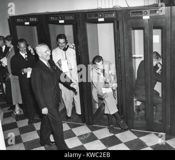 President Harry Truman walks past reporters in the telephone booths the Old State Department Building. They are reporting back to their headquarters after Truman's press conference, April 27, 1950. It was the first conference to require newsmen to remain seated and arise and identify themselves when asking questions. (BSLOC 2015 2 238) Stock Photo