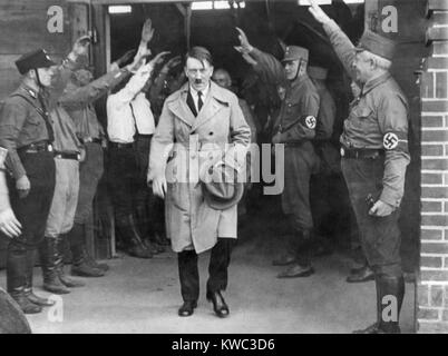 Adolf Hitler, emerging from a Nazi party meeting after a speech, 1930s. He is saluted by uniformed Storm Troopers. Hitler wears a business suit under his trench coat, suggesting the photo was taken during his early chancellorship. (BSLOC 2015 13 54) Stock Photo