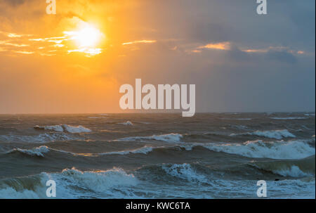 Low sun partially obscured by cloud over a rough ocean in Winter. Stock Photo