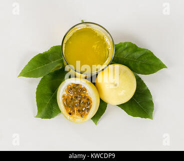 A glass of passion fruit juice and a maracuya fruit cut in half on a maracuya leaf Stock Photo