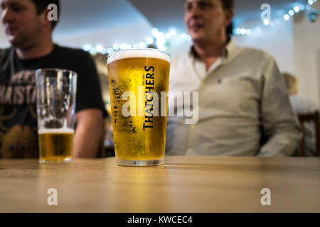 A pint glass of Thatchers Cider on a table in a bar. Stock Photo
