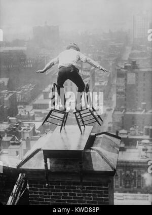 'Human Fly' John 'Jammie' Reynolds balances precariously on two tilted chairs. The dare-devil is on the roof edge of a tall Manhattan building, perched on a table placed over a chimney. Ca. 1915-1920. (BSLOC 2015 17 170) Stock Photo