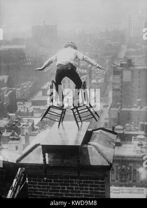 'Human Fly' John 'Jammie' Reynolds balances precariously on two tilted chairs. The dare-devil is on the roof edge of a tall Manhattan building, perched on a table placed over a chimney. Ca. 1915-1920. (BSLOC 2015 17 170) Stock Photo