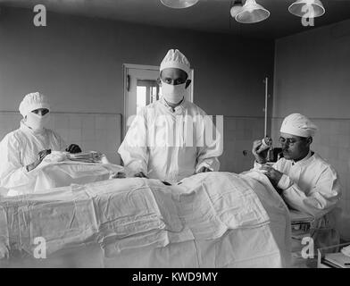 Surgical team before the operation begins, with patient is covered with sterile white cotton fabric. The anesthesiologist at right monitors patient's consciousness. 1922 in a hospital in Washington, D.C. (BSLOC 2016 10 34) Stock Photo