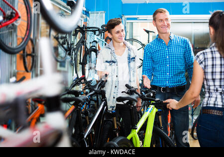 Father with happy young teenager boy asking positive female seller for help in sport bike shop Stock Photo