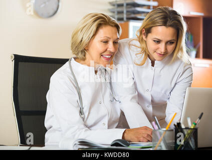 Two female doctors in white overalls working on computer at cabinet and smiling Stock Photo