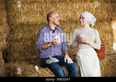 Positivel man and woman sitting together in hay and enjoying fresh milk. Focus on man Stock Photo