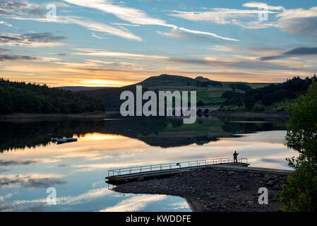 Beautiful sunset at Ladybower reservoir in the Peak District, Derbyshire, England. One man fishing from the jetty. Stock Photo