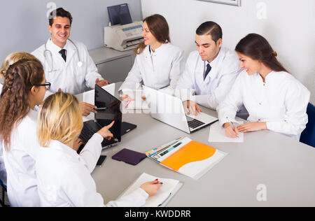 Team of positive specialists in white overalls having discussion of research work. Selective focus Stock Photo