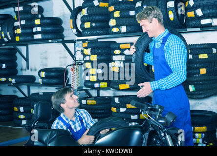 Two happy coworkers mechanics working with new tires in workshop Stock Photo