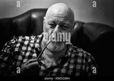 A mature male sitting in a wing back chair holding a pipe, in a reflective mood. Stock Photo