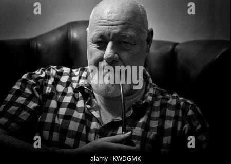 A mature male sitting in a wing back chair holding a pipe, in a reflective mood. Stock Photo