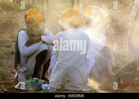 Three traders wearing orange turbans sitting by fireplace at the annual Pushkar Camel Fair, Rajasthan,India. Stock Photo