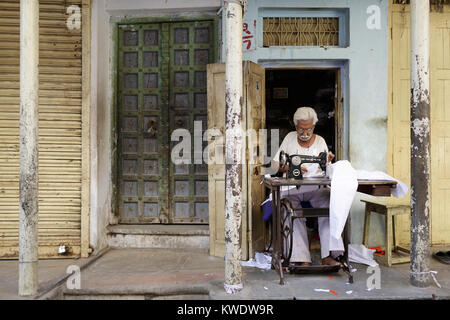 Street scene in Pushkar, Indian man in white with sewing machine outside yellow building with green doors, Rajasthan, India. Stock Photo