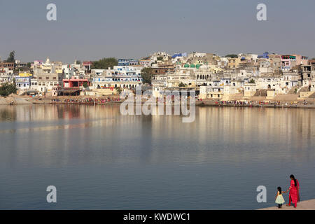 Mother and daughter in sari on the bank of the holy lake at Pushkar, Hindu pilgrims taking a ritual bath ion the other side, Rajasthan, India. Stock Photo