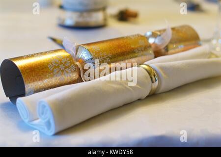 Christmas cracker alongside white napkin in a napkin ring on a white tablecloth at Christmas, UK Stock Photo