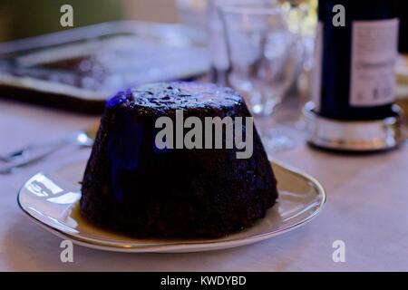 Flaming Christmas pudding on white tablecloth with drinks in the background, UK Stock Photo