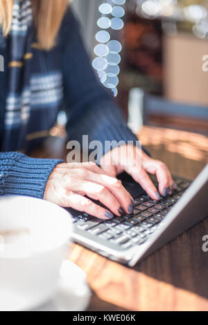 woman sitting at table in sunlight using laptop computer to shop online Stock Photo