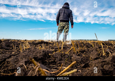 Low angle view of man wearing hooded jacket while standing on field against cloudy sky Stock Photo