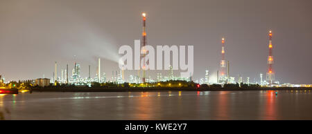 Panoramic shot of multiple oil refineries with tall gas flare stacks in the harbor of Antwerp with dirty night sky. Stock Photo