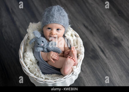 Sweet baby boy in basket, holding and hugging teddy bear, looking curiously at camera, smiling Stock Photo